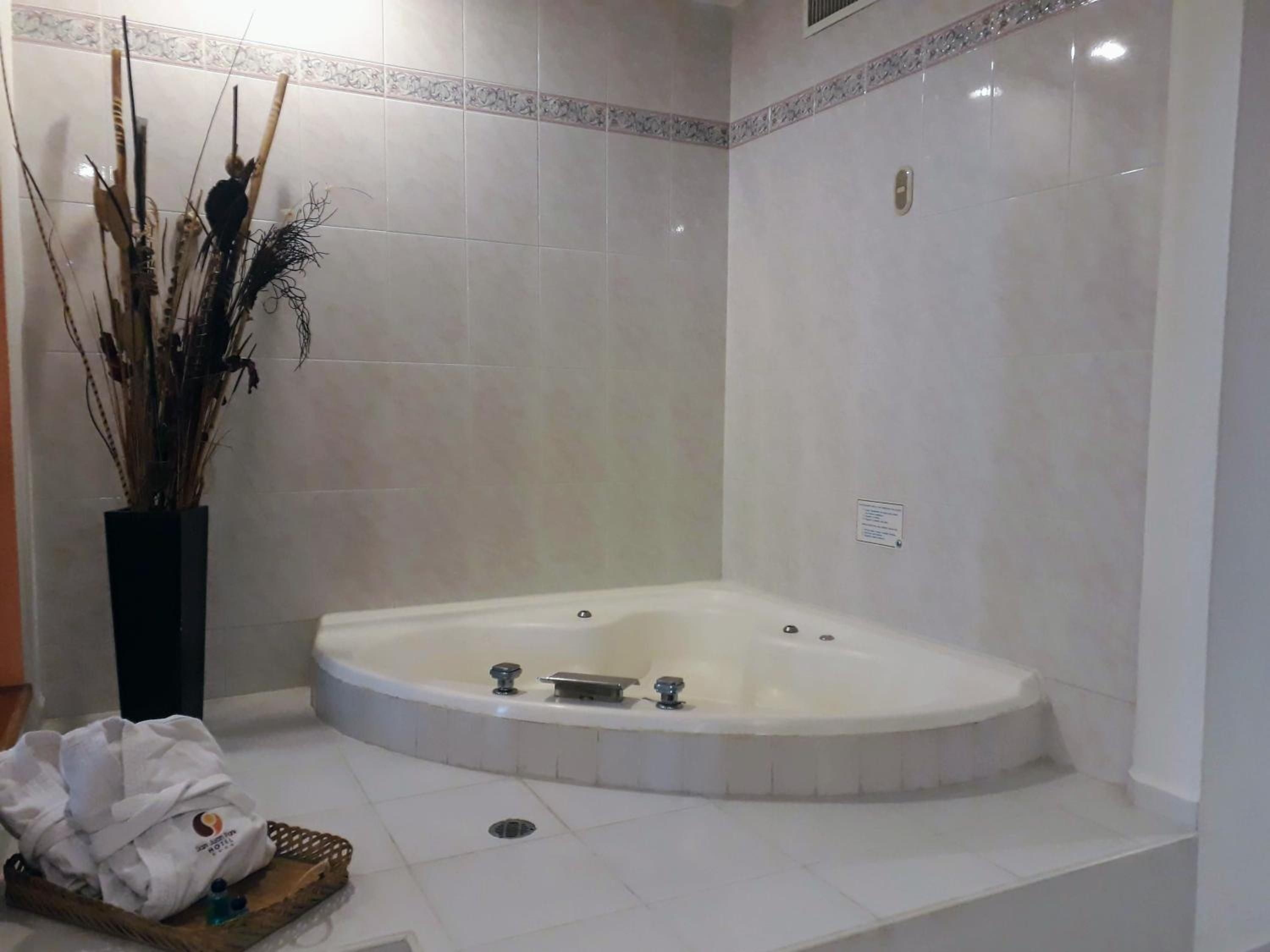 A bathroom with a freestanding bathtub, a decorative vase with dried plants, and a towel on the floor.