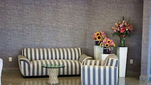 A striped sofa, a matching armchair, a glass coffee table, and two vases with flowers. - Hotel San Juan Park (San Juan del Río)