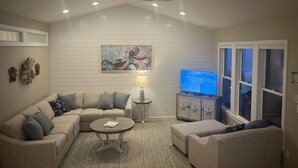 A living room with a sectional sofa, a coffee table, a TV, and a ceiling fan. - Once Upon a Tide: FULL RENO for 2026! Oceanfront, Pool, Linens (Indian Beach)