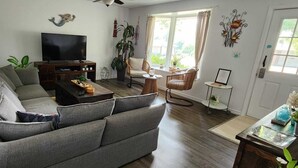 Un salon avec un canapé gris, une table basse, un téléviseur et une fenêtre avec des rideaux.