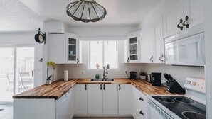 Une cuisine moderne avec des meubles blancs, un plan de travail en bois, un évier, une cuisinière et une fenêtre située au-dessus de l’évier.