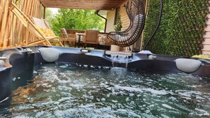 Un bain à remous doté de trois espaces de détente, entouré d’une terrasse en bois et d’un espace de repos couvert avec des chaises.