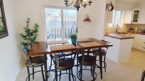 Une cuisine avec une table en bois et quatre chaises, une plante suspendue et une vue sur l’extérieur.