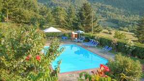 Una piscina con sillas de descanso y un pequeño pabellón, rodeada de exuberante follaje y colinas.