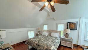 Ein Schlafzimmer mit einem großen Bett, Holzboden, Deckenventilator und einem Fenster mit Vorhängen.
