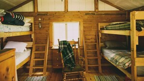 A cabin with wooden walls, bunk beds, a window, a chair, and a ladder.