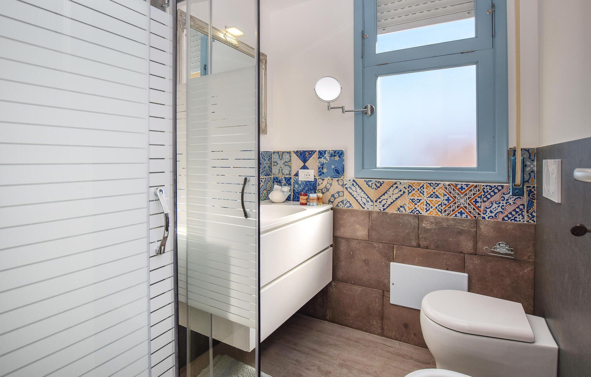 Une salle de bain avec un meuble-lavabo blanc, un miroir, une fenêtre et des toilettes.
