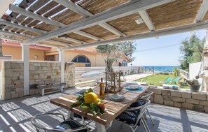 Un patio al aire libre con una mesa lista para comer, paredes de piedra y vista al mar.