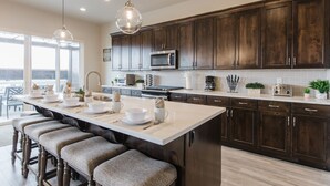 A modern kitchen with dark wood cabinets, a large island with bar stools, a microwave, and a toaster.