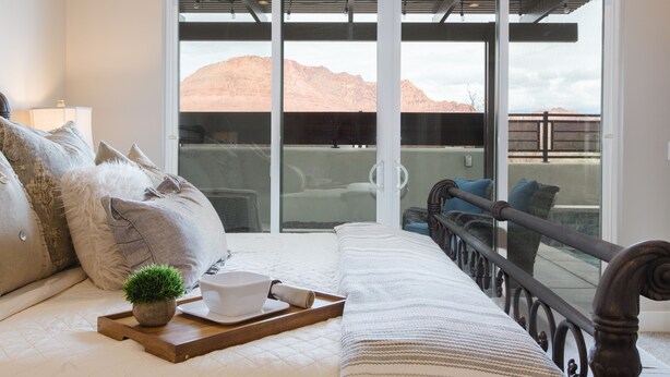 A bedroom with a bed, pillows, a tray with a plant, and a view of mountains through large sliding doors.