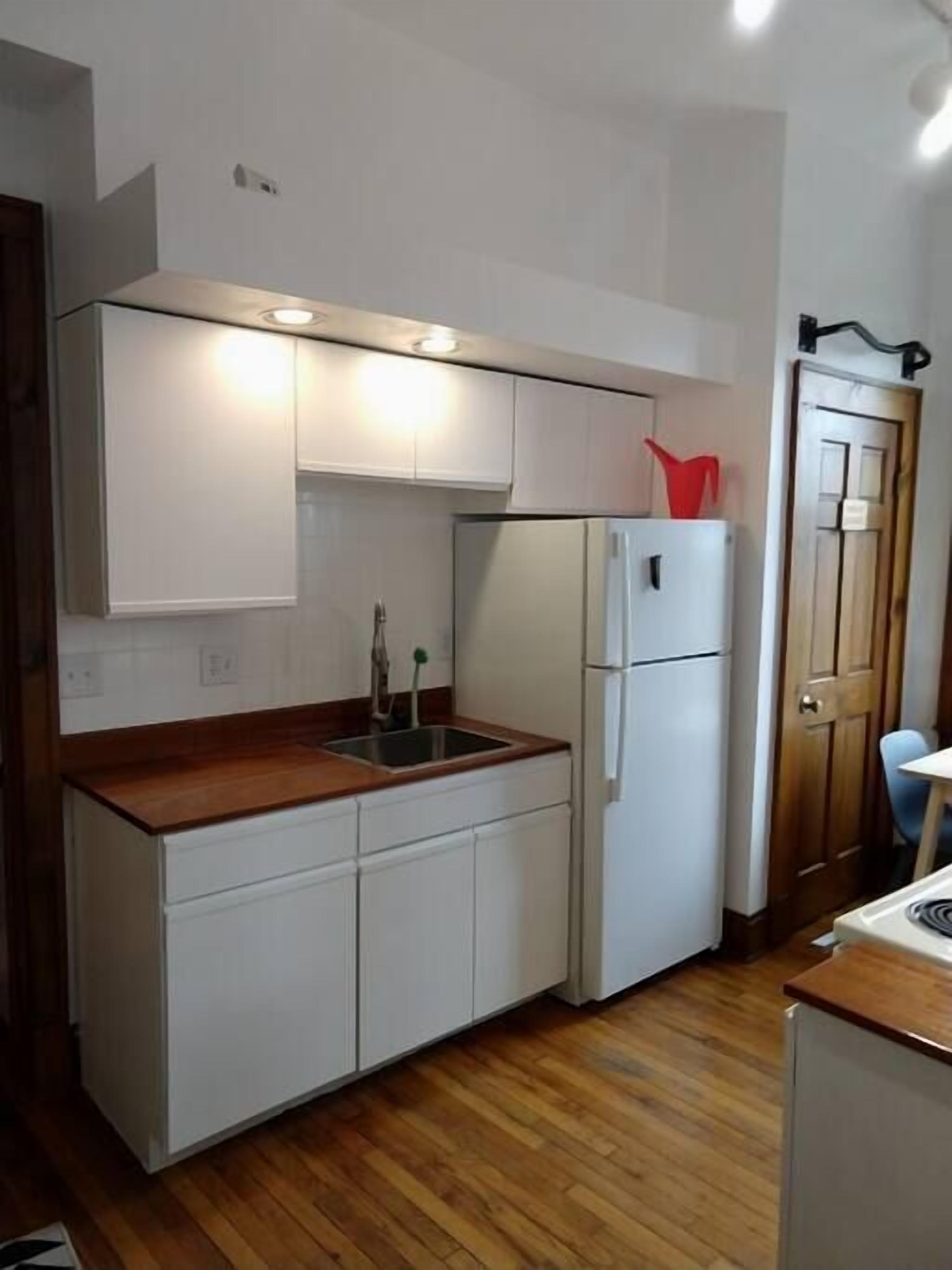 A compact kitchen with white cabinets, a wooden countertop, a sink, and a refrigerator.