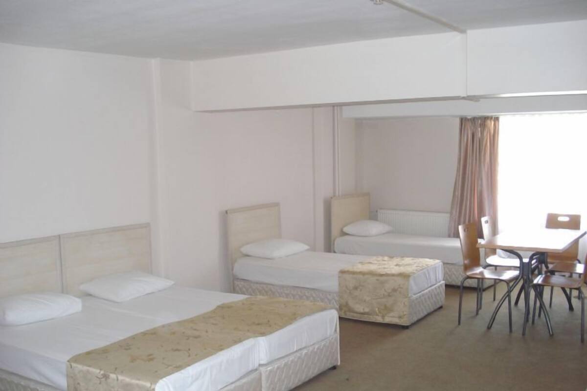 A hotel room with two single beds, a small table with chairs, and a window with curtains.
