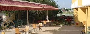 An outdoor cafe area with tables and chairs, a bicycle, and a covered seating area with a red roof.