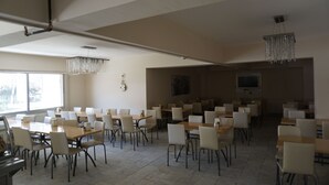 Un vaste espace dédié à la salle à manger, avec de nombreuses tables et chaises, de grandes fenêtres et un lustre.