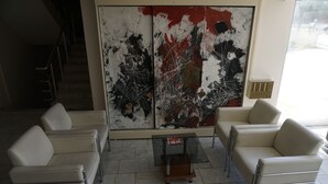 Un intérieur moderne agrémenté d’un grand tableau abstrait, de deux canapés en cuir blanc et d’une table basse en verre.