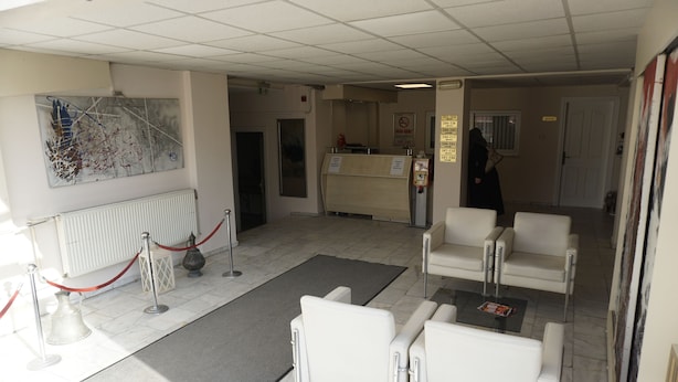 Un espace d’accueil avec un comptoir, des chaises blanches, une barrière en corde rouge et un grand tableau abstrait accroché au mur.