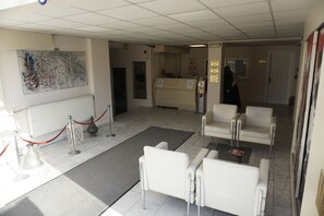 A reception area with a counter, white chairs, a red rope barrier, and a large abstract painting on the wall. - Erdogan Ege Pansiyon (Manisa)