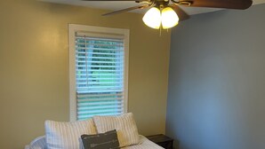 A bedroom with a bed, a ceiling fan, a window with blinds, and a nightstand. - Confluence Cabin Grafton, IL (Grafton)
