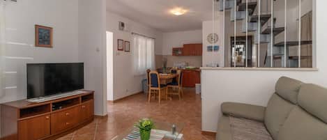 A living room with a TV, sofa, and a dining area with chairs and a table.