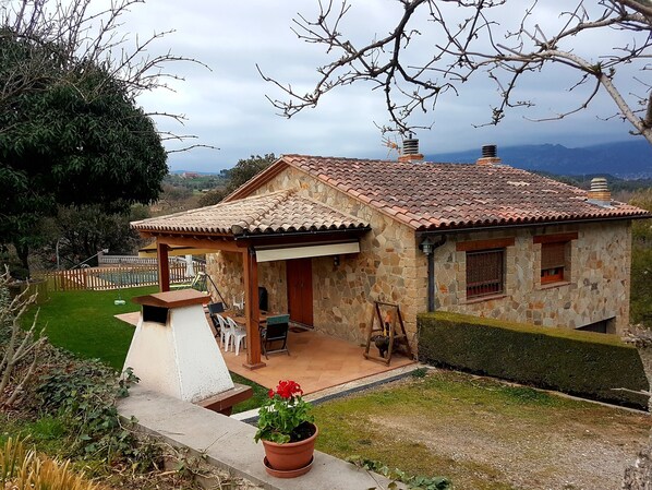 Situated in a lush green setting, this charming cottage features a patio area with outdoor seating and a small garden.