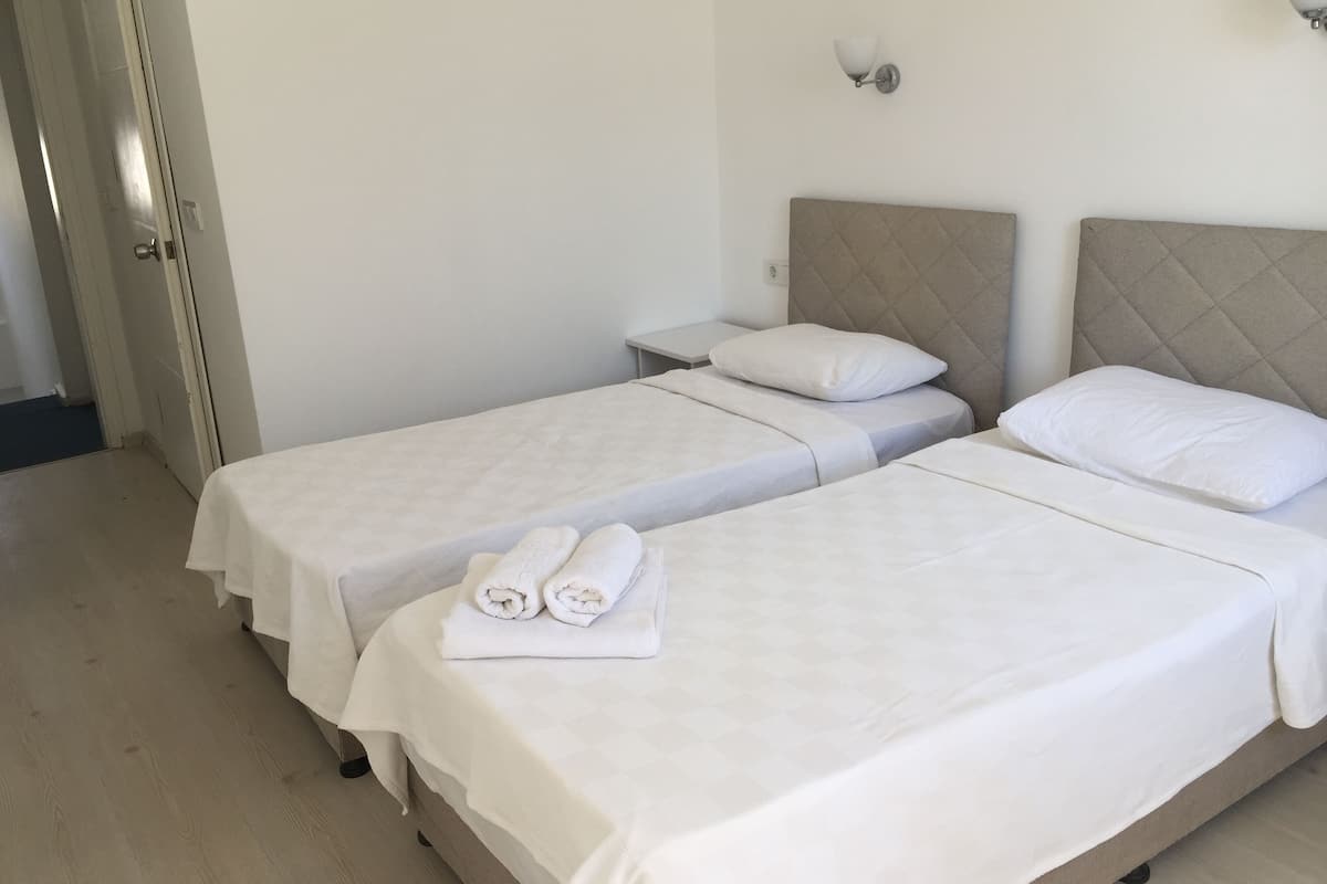 A hotel room with two single beds, a bedside table, and a wall-mounted light fixture.