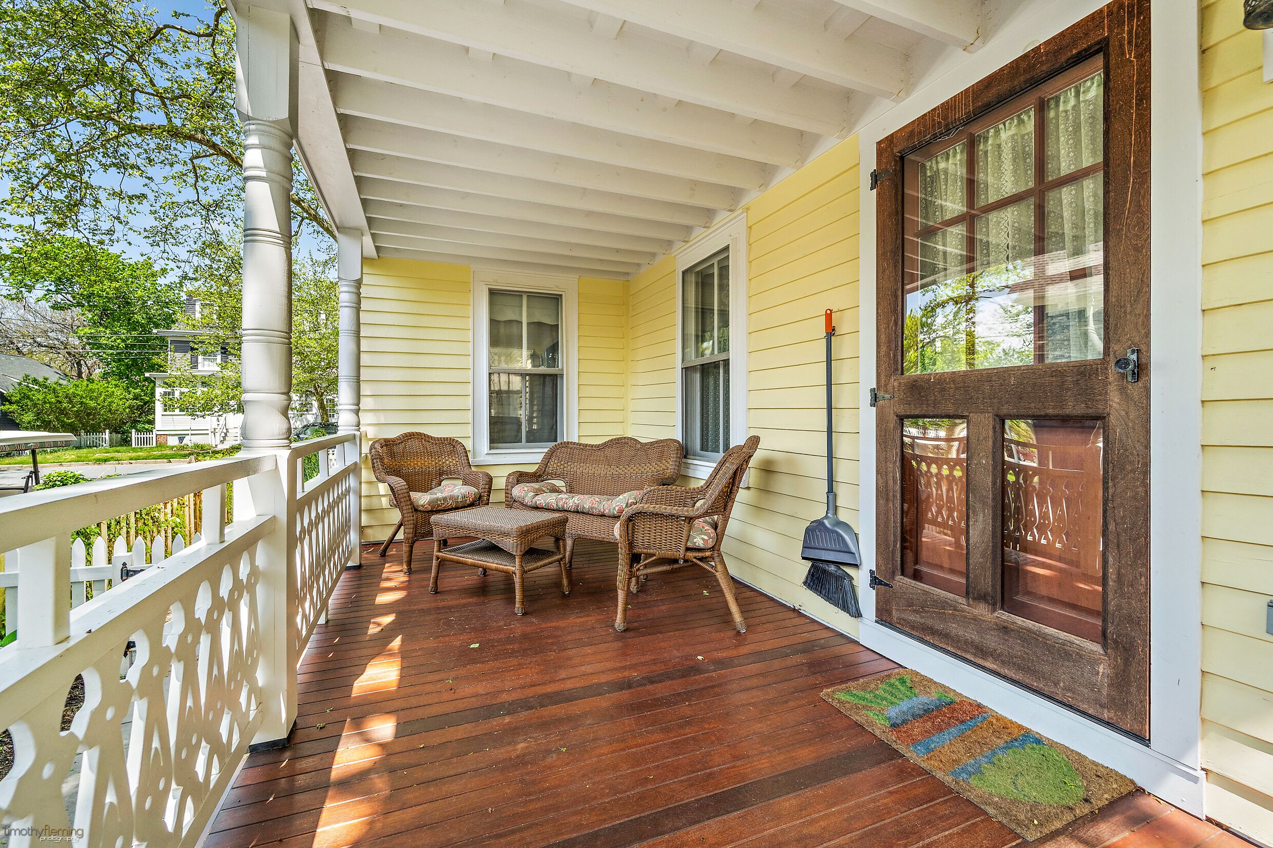 A porch with wooden flooring, wicker furniture, and a white railing.