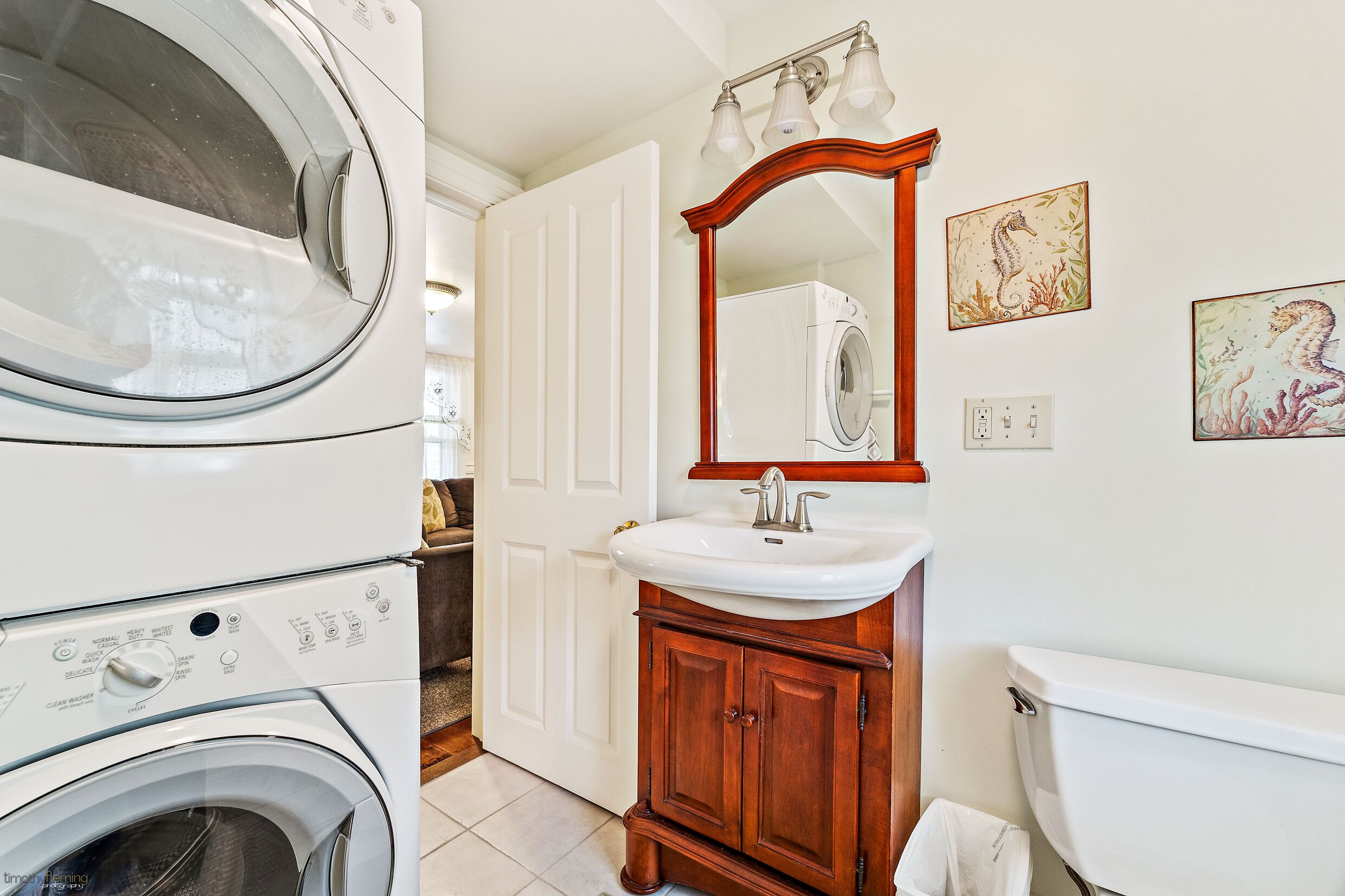 A laundry room with a front-loading washing machine, a sink with a wooden cabinet, and a mirror above it.