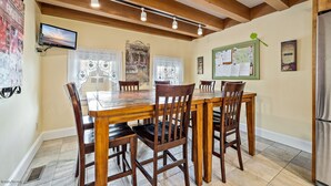 A dining area with a wooden table and chairs, a mounted TV, and a bulletin board with papers. - Sea Horse Cottage-5 Bedrooms, 3 Full Baths, 2 Half Baths, Sleeps 14 (West Cape May)