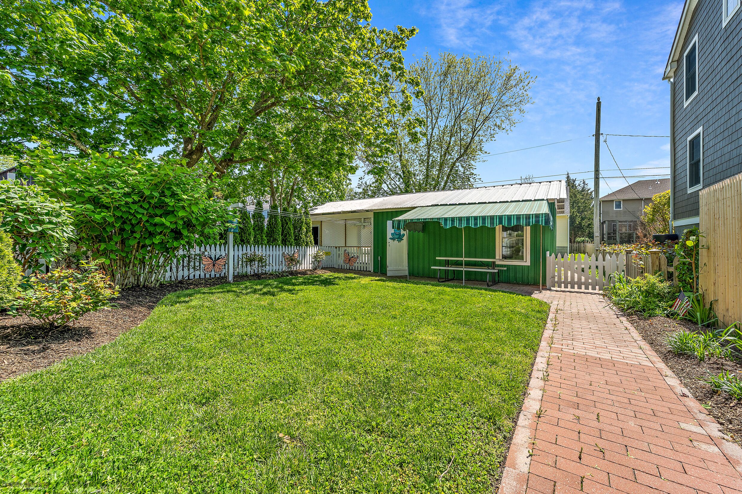 A well-maintained backyard with a green shed, a brick pathway, and a white picket fence.