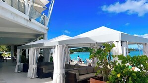 A covered outdoor seating area with sofas and potted plants, overlooking a pool and beach. - Lovely Sapphire Beachfront Condo - Snorkel Crystal Cove - Paradise ! (St Thomas)