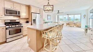 A spacious kitchen with modern appliances, a large island with bar stools, and a view of the outdoors through large windows. - Lovely Sapphire Beachfront Condo - Snorkel Crystal Cove - Paradise ! (St Thomas)