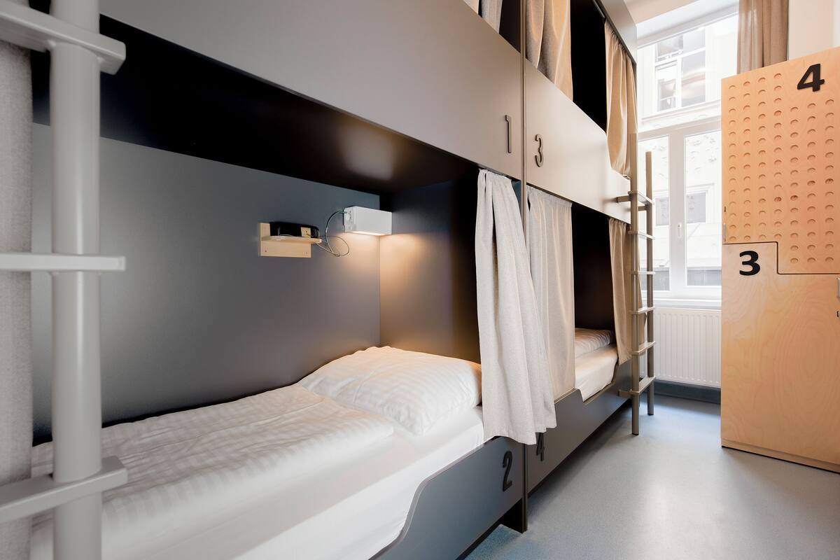 Een slaapkamer met stapelbed, raam, een wandplank en een deur met genummerde panelen.