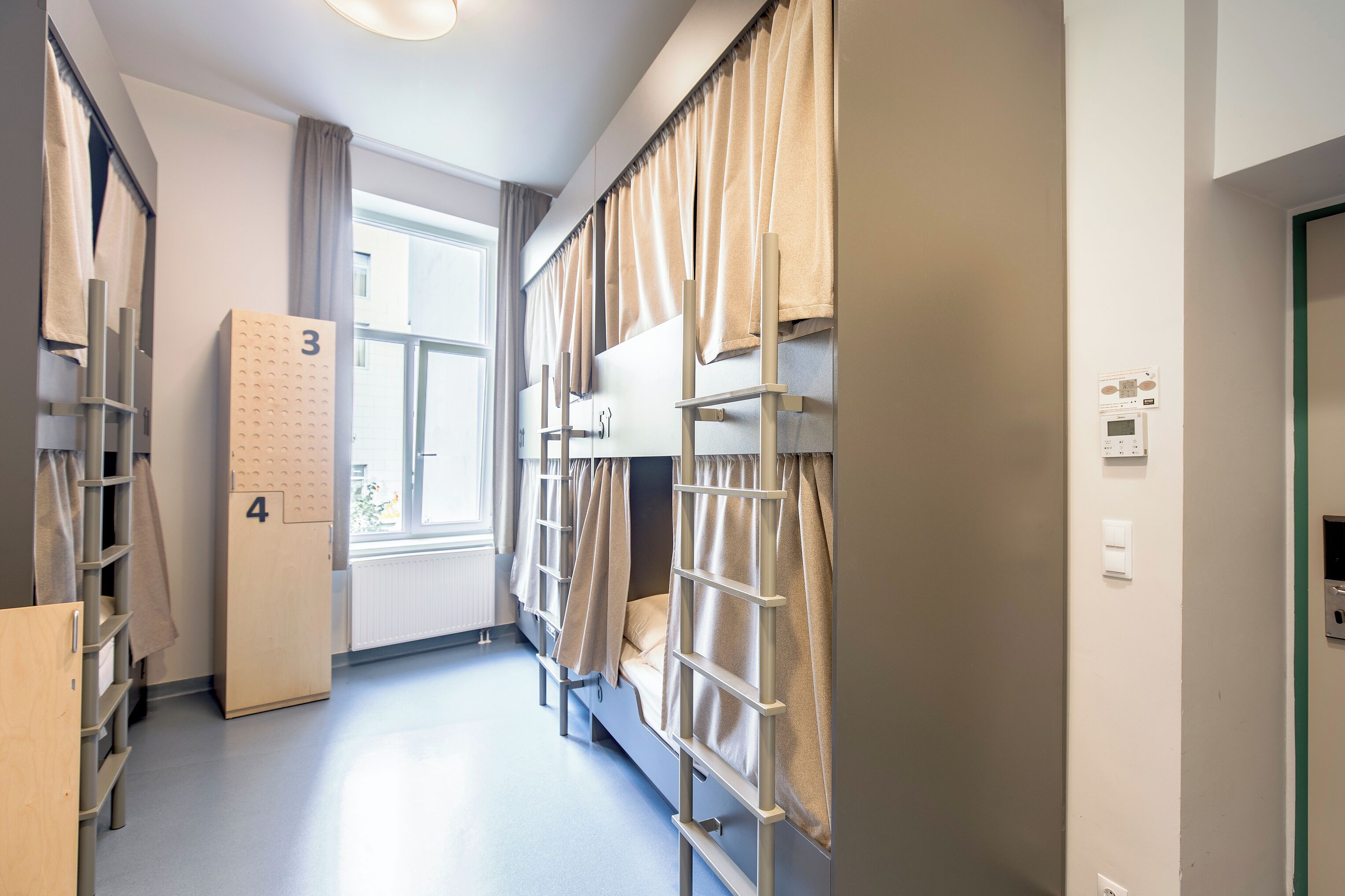 A dormitory room with bunk beds, a wardrobe, and a window with curtains.