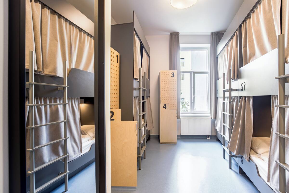 Een slaapzaal met stapelbedden, genummerde opbergkasten en een raam met gordijnen.