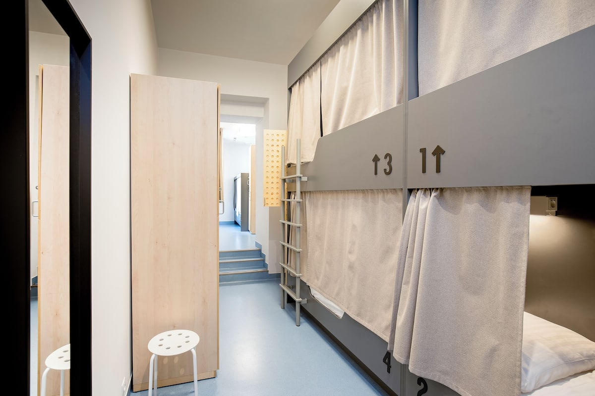 Een hotelkamer met stapelbedden, een klein wit krukje en een trap naar een ander gedeelte.
