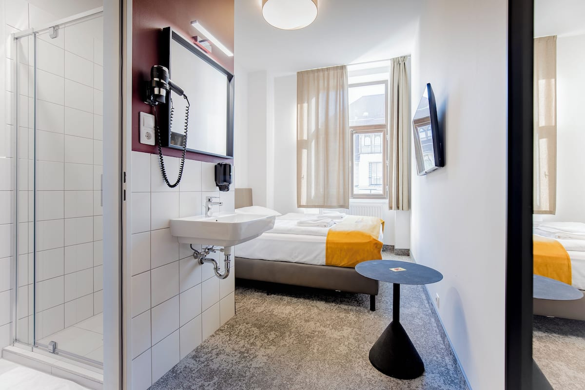 Een hotelkamer met een bed, nachtkastje, spiegel, wastafel en douche.