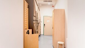 Un couloir avec des casiers numérotés 3 et 4, un petit tabouret et une porte dotée d’un cadre vert.