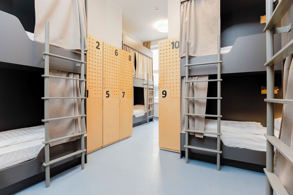 Een slaapzaal met stapelbedden, genummerde kastjes en een ladder.