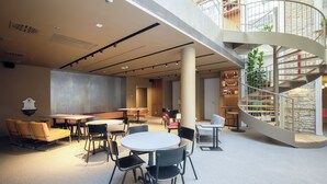 Un intérieur moderne avec un escalier en colimaçon, des tables et des chaises rondes, et une grande plante.