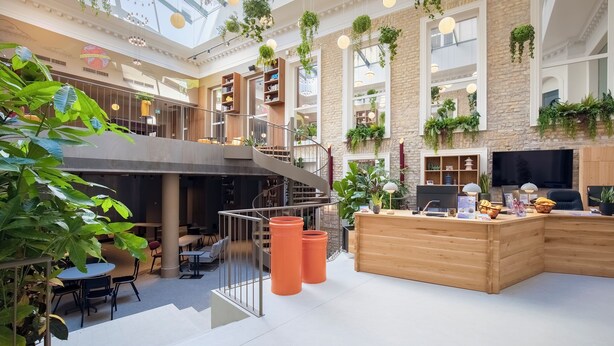 Un vaste espace intérieur doté d’un escalier central, d’un comptoir d’accueil en bois et de plusieurs coins salon.