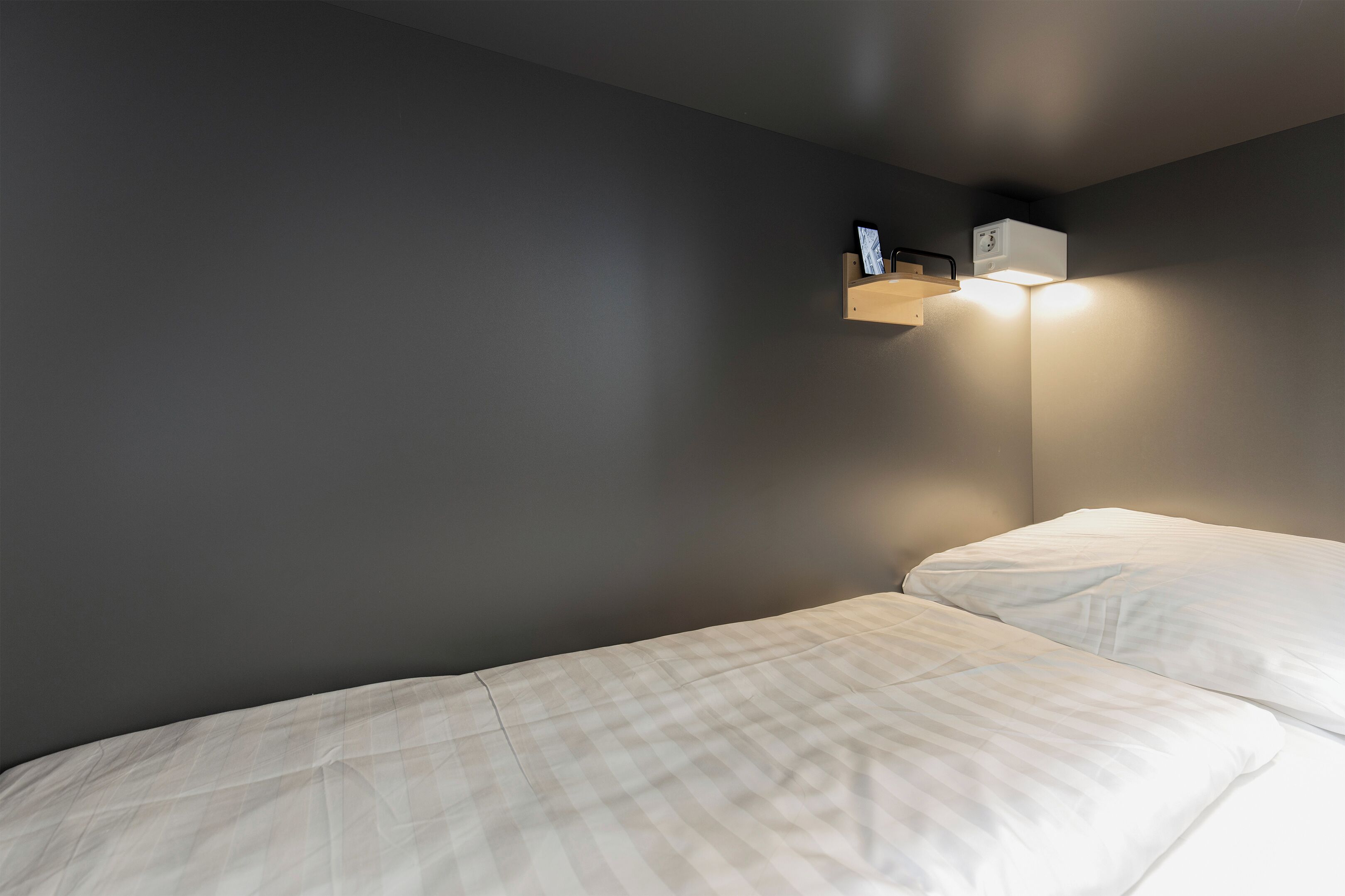 Une chambre avec un lit simple, une table de chevet et un luminaire fixé au mur.