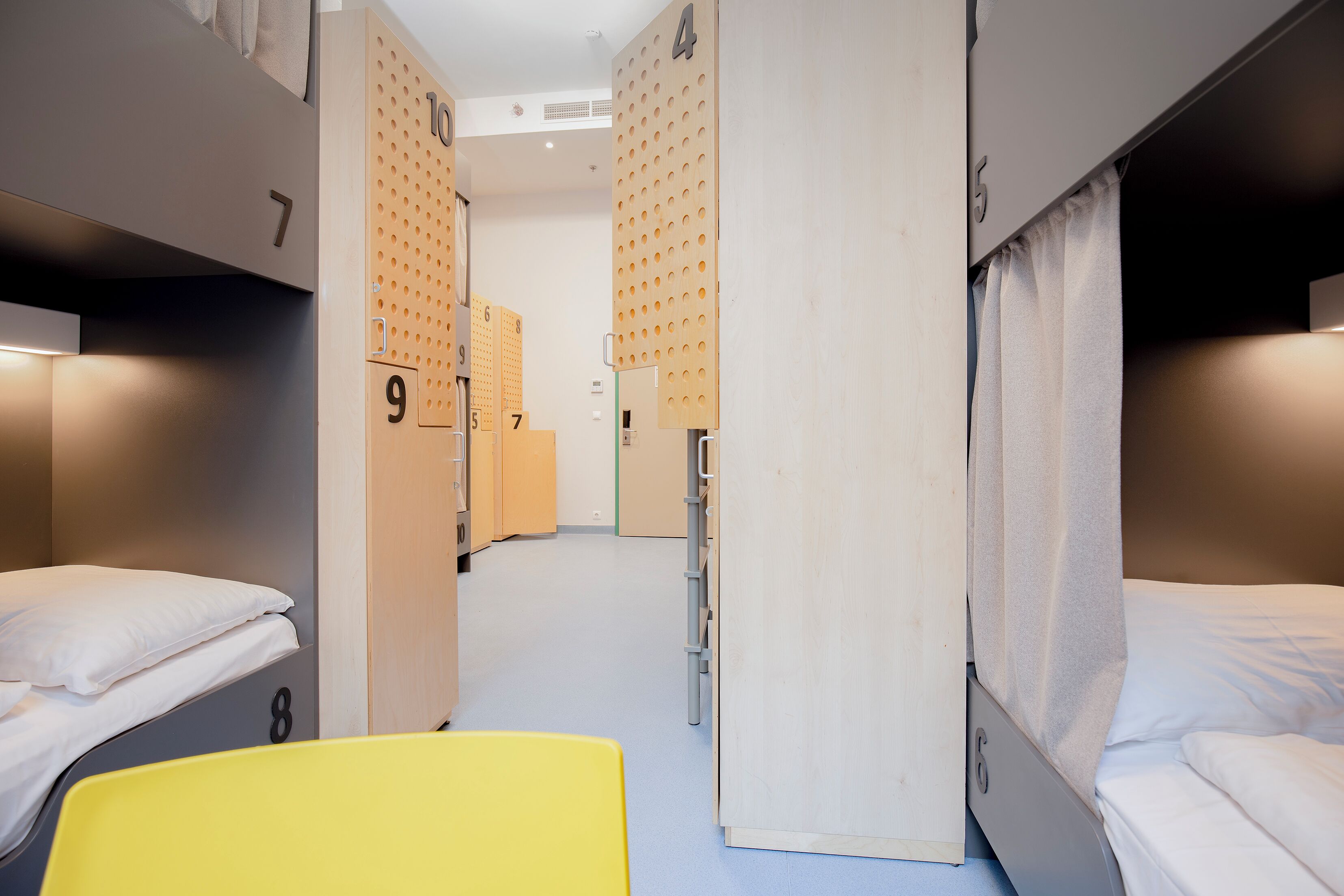Una habitación de hotel con literas, una silla amarilla y una pared de madera con paneles numerados.