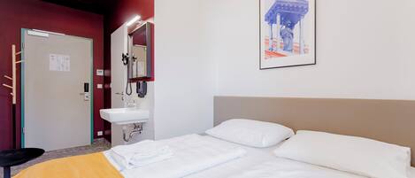 Habitación de hotel con cama, baño con lavamanos y puerta con espejo.