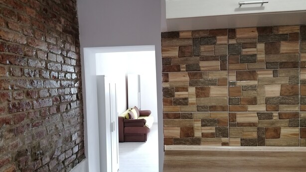 A hallway with a brick wall, a wooden floor, and a stone wall with a sofa and cushions. - Courage place is sunny (Cluj-Napoca)