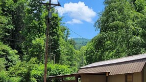 A rustic cabin by a flowing stream, surrounded by lush greenery and a clear sky.