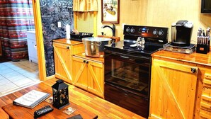 A cozy kitchen with wooden cabinets, a stove, a coffee maker, and a welcome sign.