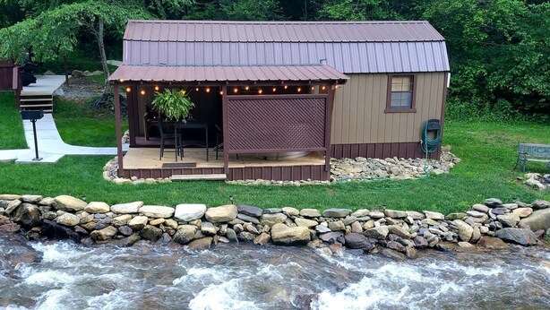 A riverside cabin with a deck, a covered outdoor seating area, and a small window.