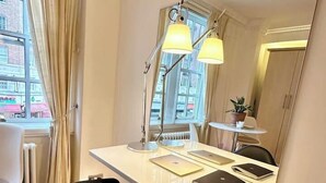 Une chambre moderne avec un bureau blanc, une chaise noire et un grand miroir. Il y a deux lampes sur le bureau et une fenêtre avec des rideaux.