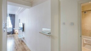 Un couloir avec un téléviseur à écran plat fixé au mur, une petite étagère et une porte donnant sur une salle de bain.