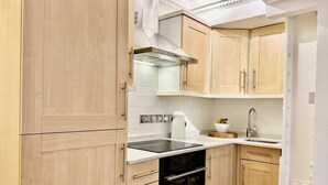 Une cuisine de taille réduite, avec des meubles de rangement en bois, une cuisinière noire, un plan de travail blanc et un évier.